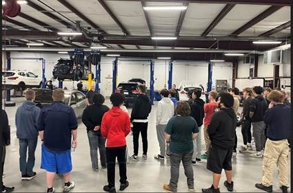 Several high school students listening to an instructor in an auto mechanics garage